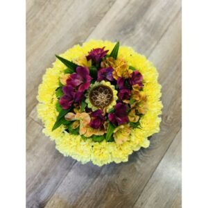 A floral arrangement with yellow flowers surrounding a cluster of purple and brownish flowers, displayed on a wooden floor, serves as a Table Centerpiece With Candle decoration.