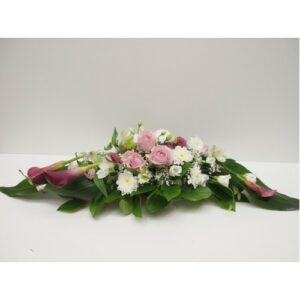 An arrangement of pink roses, white flowers, and green foliage on a plain background forms a Classic Love Petite Casket Spray for sympathy.