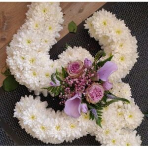 OM in the shape of the letter 'j' with white blooms and a cluster of purple flowers and greenery, symbolizing spirituality.