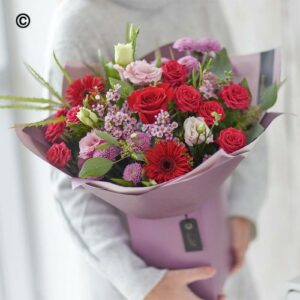 Person holding a Valentines Box wrapped in purple paper as a Valentine's Day gift.