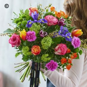 A person holding a vibrant Deluxe Spring Bouquet of assorted flowers.