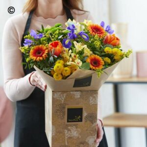 Florist holding a vibrant Mixed Spring Handtied bouquet, wrapped in decorative paper.