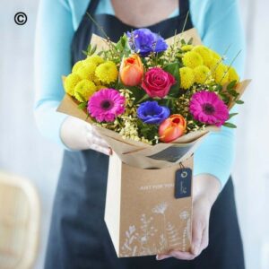 A person holding a Spring Hand Tied Bouquet of spring flowers wrapped in brown paper with a "just for you" tag.
