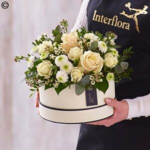 Florist holding a bouquet of cream roses and greenery arranged in a Hat Box Deluxe.