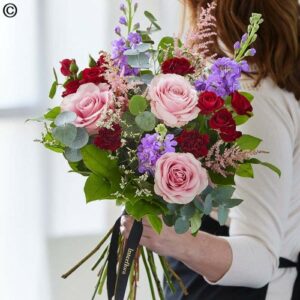 Person holding a Hand Tie Bouquet Spring of pink roses and assorted purple flowers.