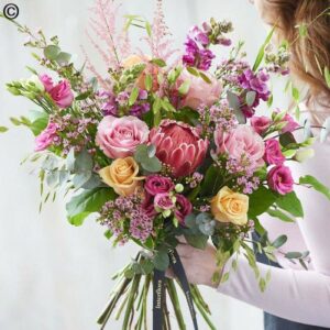 A person holding a Mixed Rose Garden Hand Tie of assorted flowers including mixed roses and a protea.