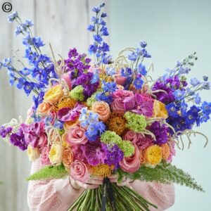 A vibrant Hand Tie Wild of wild flowers in various shades of blue, purple, pink, and yellow, wrapped in pink fabric.