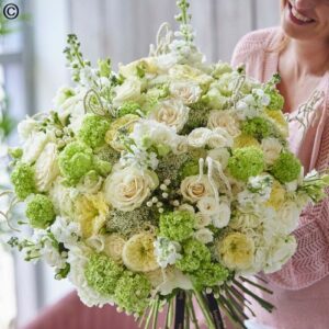 A cheerful person holding a Hand Tie Deluxe White bouquet of white and green flowers.