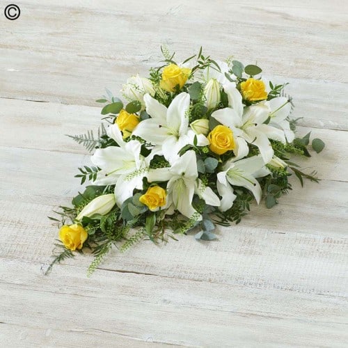 A bouquet of white lilies and yellow roses arranged on a wooden surface, featuring Oasis Spray Whites and Yellows.