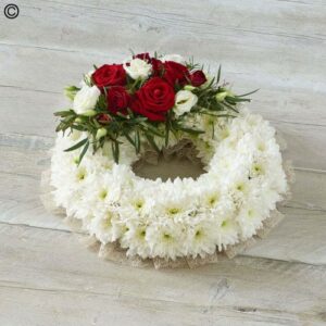 Traditional Funeral Wreath: A traditional funeral wreath featuring a circle of white flowers with a bouquet of red roses and green foliage at the center.