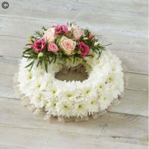 Traditional  Funeral Wreath with white chrysanthemums and pink roses on a wooden surface.