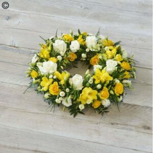 A Yellow and Cream Wreath featuring flowers on a wooden surface.