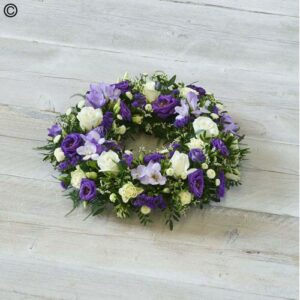 A sympathy Purple and White Wreath on a wooden surface.