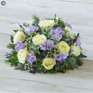 A Lilac and Lemon Posy featuring lemon yellow roses, lilac flowers, and greenery on a wooden surface.