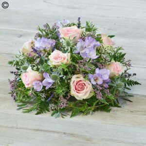A bouquet of Purple and Pink Posy arranged with greenery on a wooden surface.
