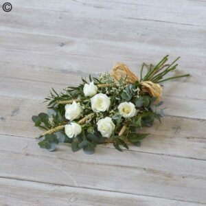 A White Rose Tied Sheave of white roses and green foliage on a wooden floor.