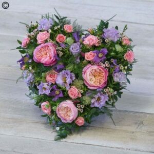 Pastel Heart-shaped floral arrangement with pink roses and purple accents in pastel colors on a wooden surface.