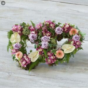 Floral arrangement in the shape of a Pastel Open Double Heart featuring purple roses and pink accents.