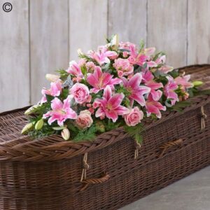 A Wicker Pink Rose and Lily Casket Spray adorned with a spray of funeral flowers including pink roses and lilies.