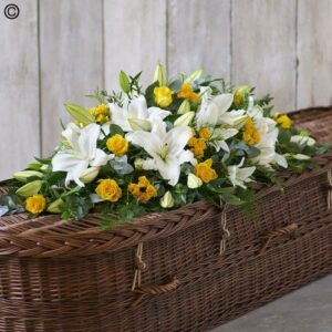 A Yellow and White Casket Spray adorned with a sympathy flower arrangement of white lilies and yellow roses.