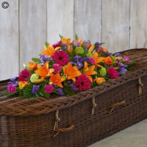 A Vivid Casket Spray on top of a wicker casket.