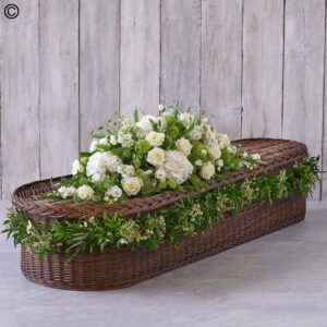 A White Country Garden Casket Spray adorned with a floral arrangement of white roses and green foliage against a wooden backdrop.