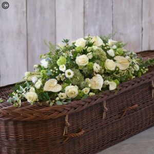 A Simply White Casket Spray with white roses on a wicker casket.