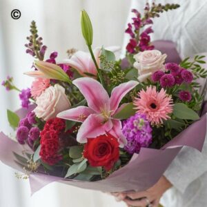 A person holding a Valentines Handtie of mixed flowers including lilies, roses, and gerberas.
