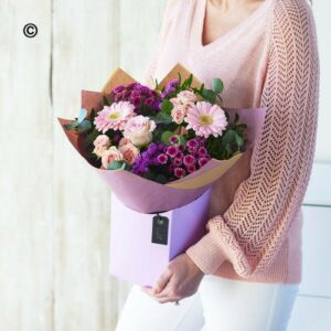 Woman holding a bouquet of pink and purple flowers wrapped in Pastel Box.