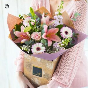 Woman holding a Peach Handtie bouquet of mixed flowers in gift packaging.