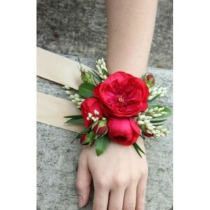 A floral corsage with red roses and white blossoms worn on a wrist, perfect for Wedding planning.