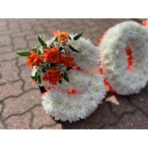 Floral arrangement designed to resemble a pair of Letter Classic White shoes, placed on a paved surface.