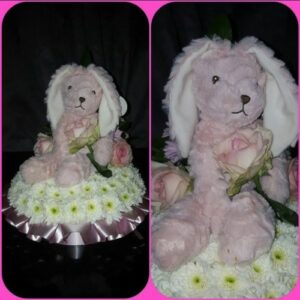 A plush pink poodle toy seated amidst white and pink floral decorations, showcased from two angles alongside a Posy With a Bear.