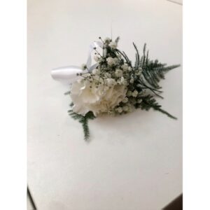 A white floral boutonniere with greenery on a white surface, perfect for Wedding planning.
