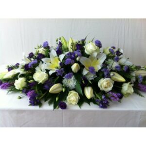 An elegant Casket Spray featuring white roses, lilies, and purple accent flowers.